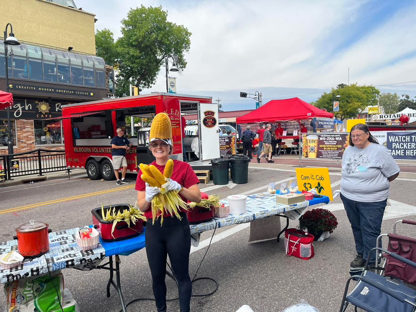 A festival volunteer holding fresh sweet corn at a downtown food stand